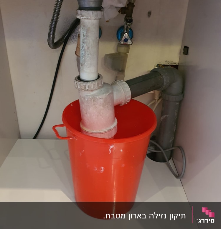 דלי אדום מתחת לצנרת כיור במטבח